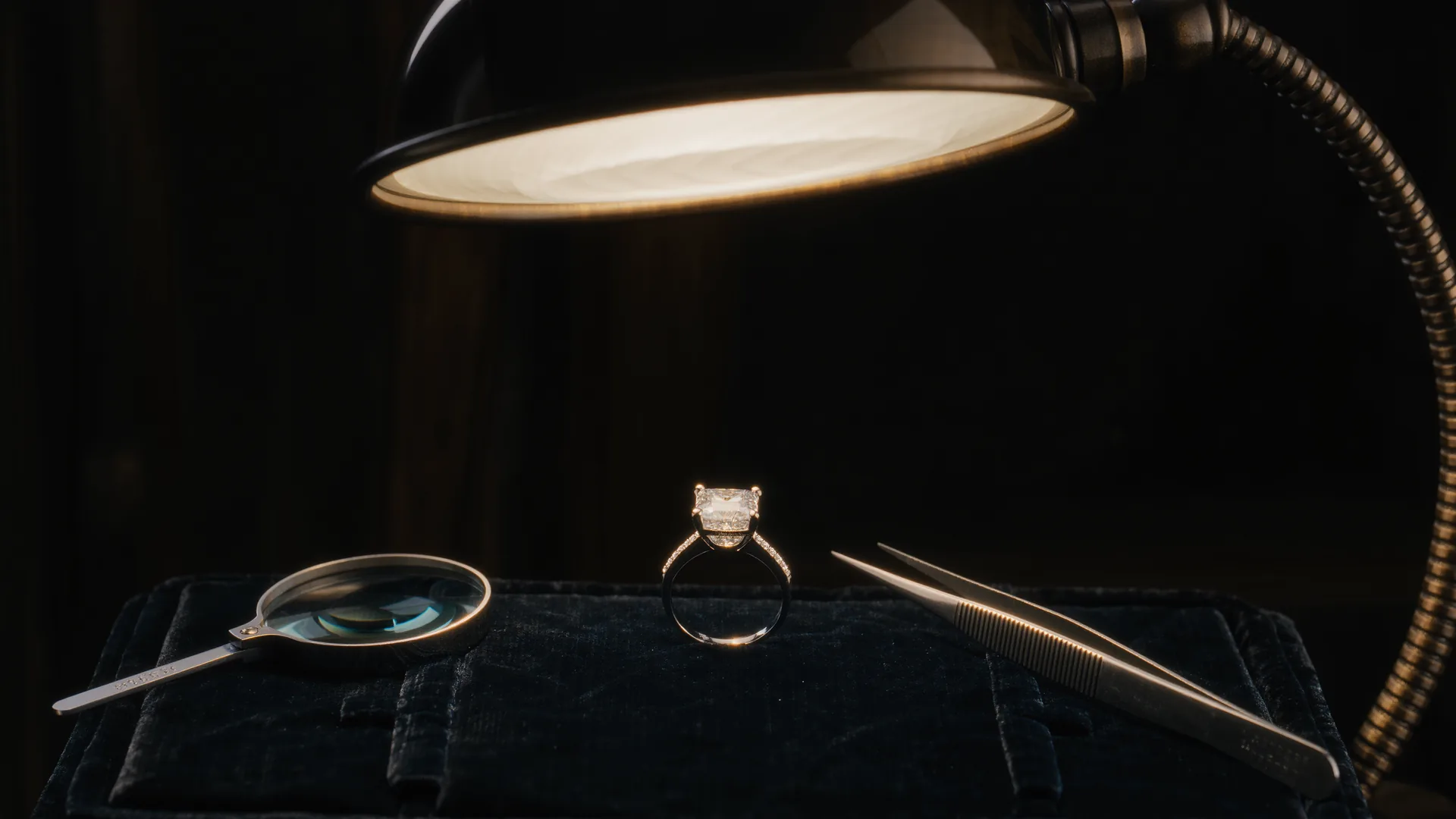 Diamantring auf schwarzem Samt unter der Juwelierlampe, daneben Lupe und Pinzette