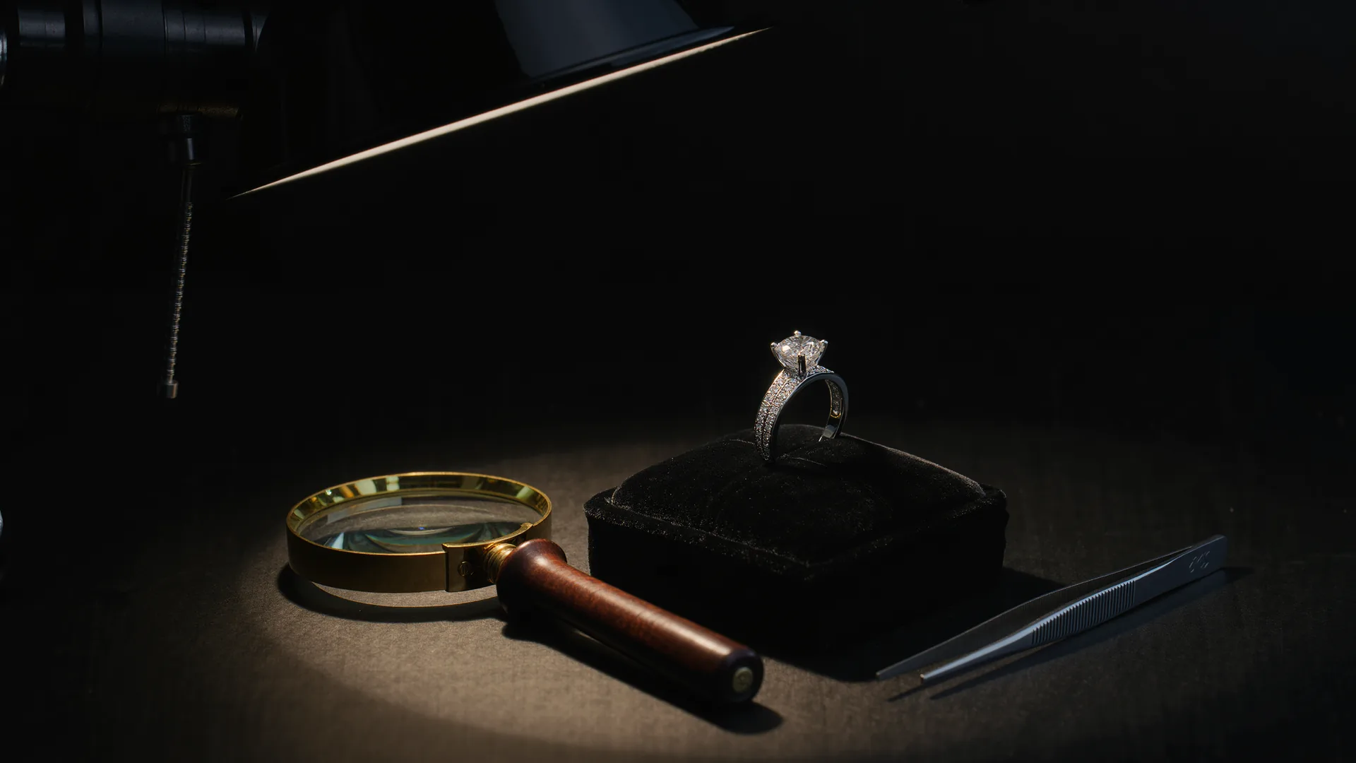 Diamantring auf schwarzem Samt unter der Juwelierlampe, daneben Lupe und Pinzette
