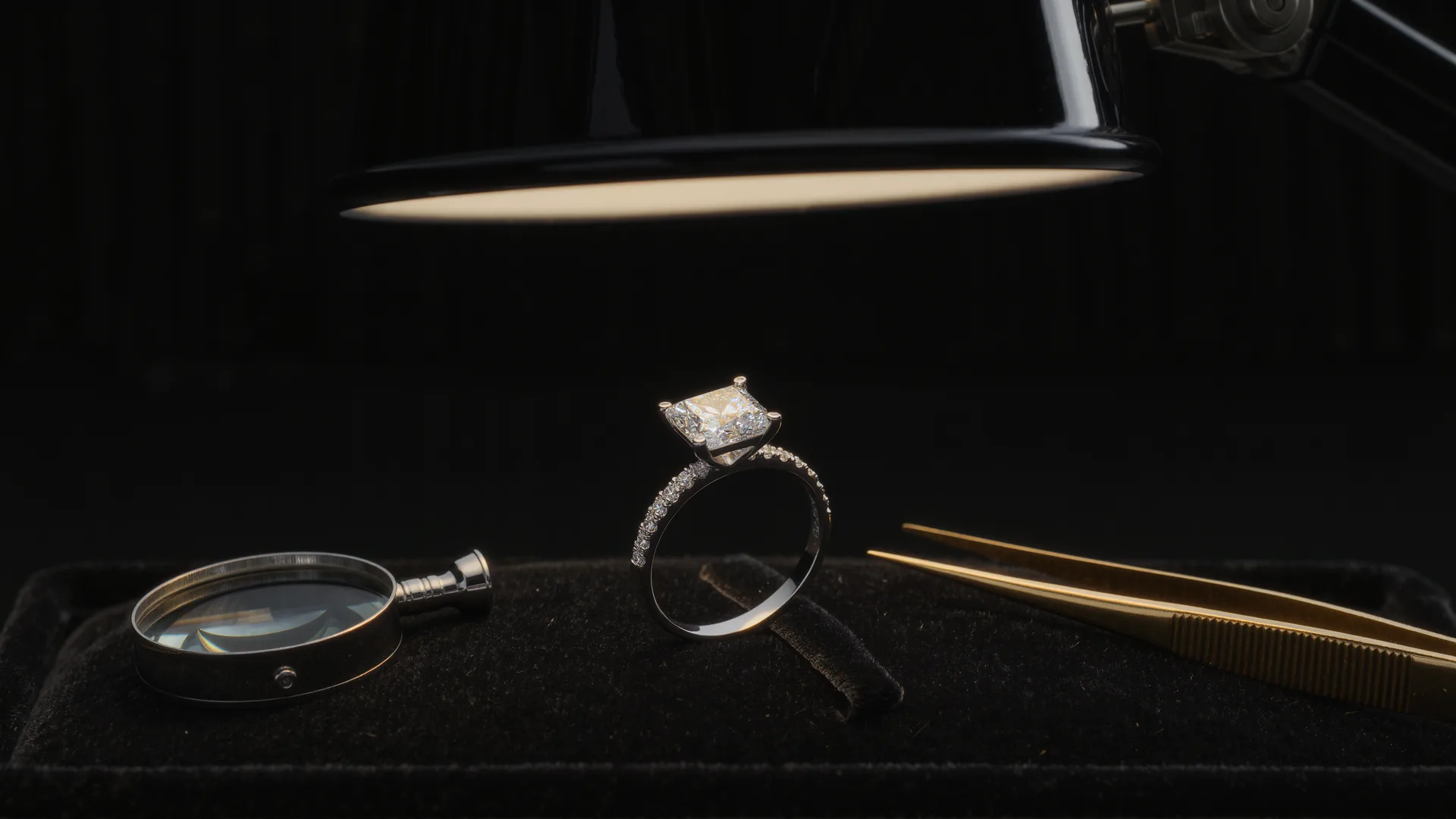 Diamantring auf schwarzem Samt unter der Juwelierlampe, daneben Lupe und Pinzette