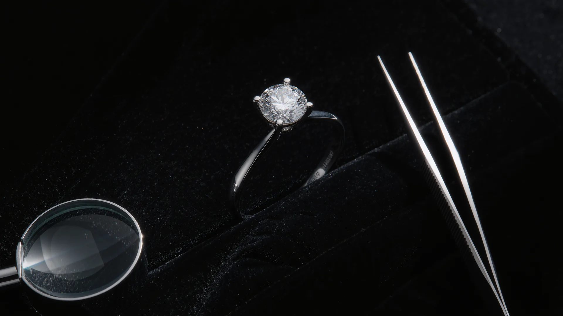 Diamantring auf schwarzem Samt unter der Juwelierlampe, daneben Lupe und Pinzette