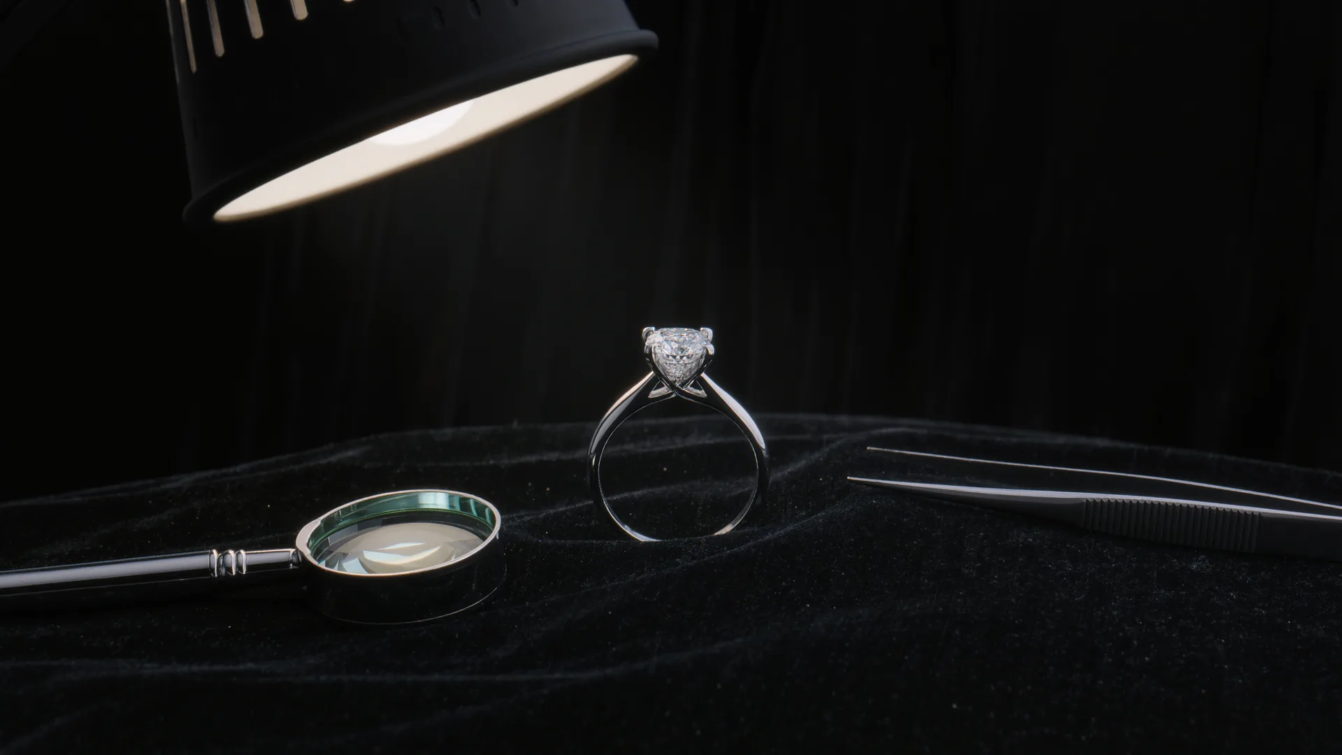 Diamantring auf schwarzem Samt unter der Juwelierlampe, daneben Lupe und Pinzette