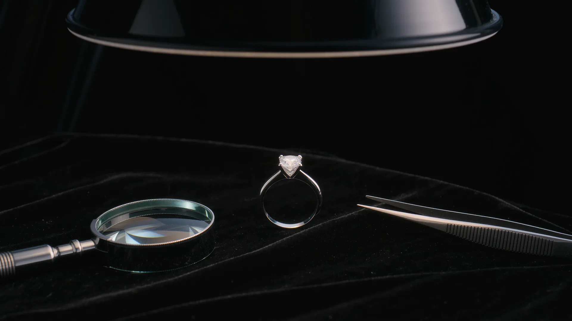 Diamantring auf schwarzem Samt unter der Juwelierlampe, daneben Lupe und Pinzette